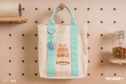 LuLu The Piggy Caturday tote bag hanging on peg board with keychain and cartoon pig and piglet details.