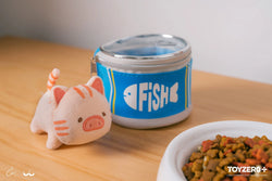 Kitty plush keychain next to cat toy and food bowl, stuffed animal by jar and table, with playful elements.