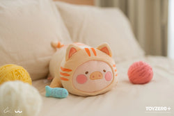 Stuffed pig toy in cat garment on bed, with ball of yarn nearby.